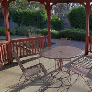 An outdoor gazebo with a metal table and chairs, offering a shady spot to relax with a garden view.