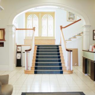 A bright and elegant hallway featuring a central staircase with a blue carpet.