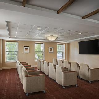 A cozy meeting room with comfortable seating arranged in rows, facing a large television, ideal for presentations or group gatherings.