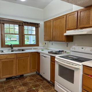 A cozy kitchen featuring wooden cabinets, essential appliances, and natural light from the windows.