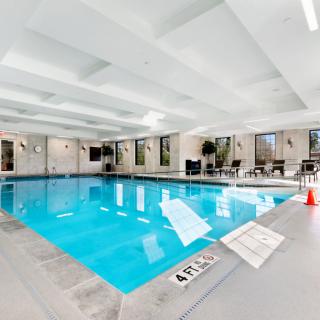 A bright indoor swimming pool area with lounge chairs and large windows.