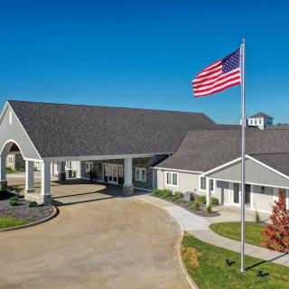 A modern building with an American flag flying nearby, framed by a clear blue sky and neatly maintained landscaping.
