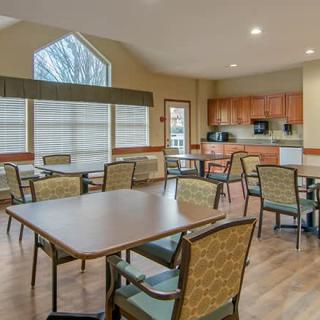 A spacious dining and kitchen area with several tables and chairs, featuring large windows and wooden flooring.