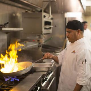 A chef skillfully cooks with flames in a professional kitchen.