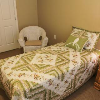A cozy bedroom with a single bed featuring a patterned quilt and a decorative pillow, accompanied by a wicker chair.