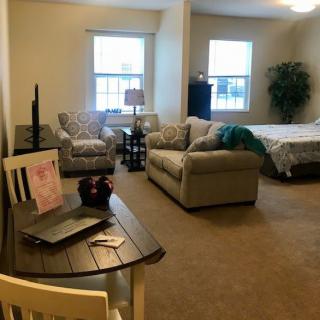 A cozy studio apartment with a combined living and sleeping area, featuring a sofa, bed, small table with a laptop, and large windows.