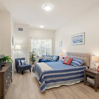 A modern bedroom with striped bedding, decorated with contemporary furniture and plants.
