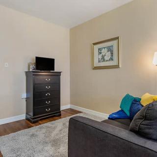A cozy living room corner featuring a dresser with a TV on top, a sofa with colorful cushions, and a framed artwork on the wall.