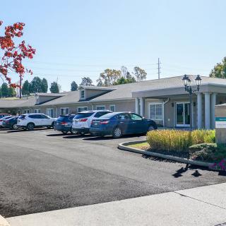 A sunny view of a parking lot in front of a motel with several parked cars and surrounding trees.