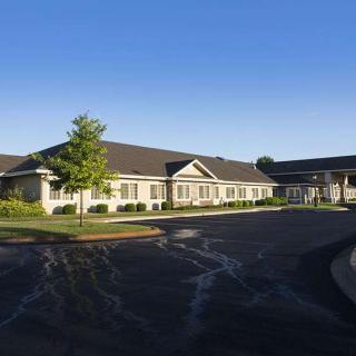 A wide view of a single-story building with a large parking area in front, set against a clear blue sky.