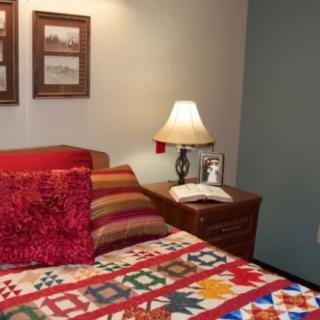 A cozy bedroom with a colorful quilt, decorative pillows, and a lamp on the nightstand.