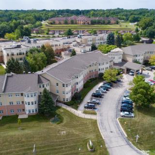 Aerial view of a complex with multiple buildings surrounded by greenery and a parking area.