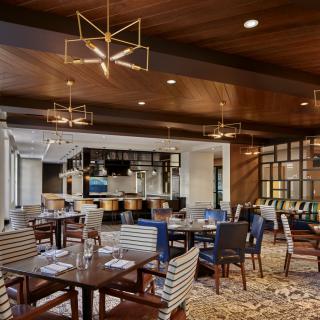 A modern restaurant dining area featuring stylish chandeliers, wood paneling, and a well-equipped bar.