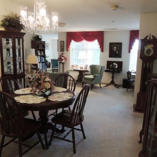 A cozy, traditionally decorated dining and living area featuring a chandelier, wooden furniture, and elegant curtains.