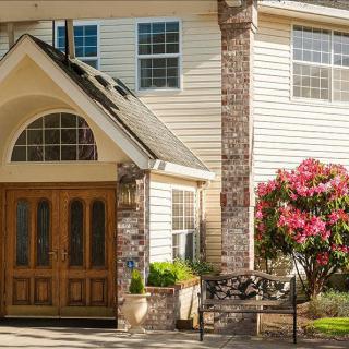 A welcoming house entrance with a wooden double door and well-maintained landscaping, including blossoming flowers.