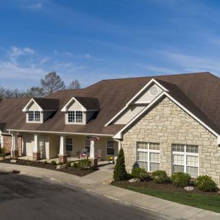 A spacious residential house with a stone facade and landscaped driveway under a clear blue sky.
