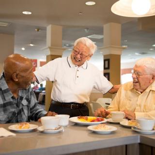 A group of senior men enjoying a meal and engaging in lively conversation at a dining table.