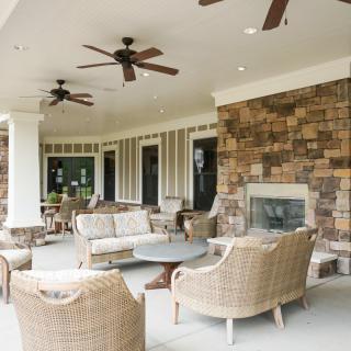 A cozy outdoor patio with wicker furniture, ceiling fans, and a stone fireplace.