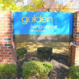 A sign for the Golden Living Center surrounded by a brick structure and greenery.