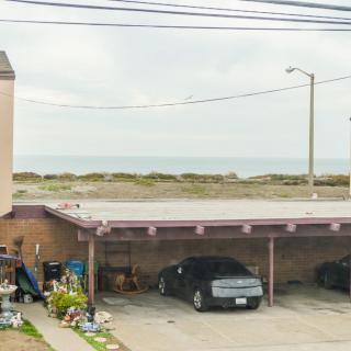 A small carport with parked cars and a view of the ocean in the background under a cloudy sky.