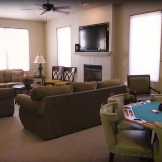A cozy living room featuring comfortable sofas, a wall-mounted television, a fireplace, and a card table.