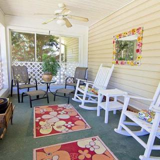 A cozy porch featuring rocking chairs, colorful rugs, and a ceiling fan, perfect for relaxing outdoors.