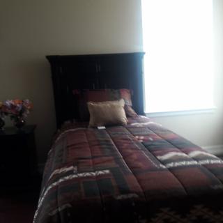 A cozy bedroom with a single bed, plaid comforter, and soft pillows next to a nightstand with flowers.
