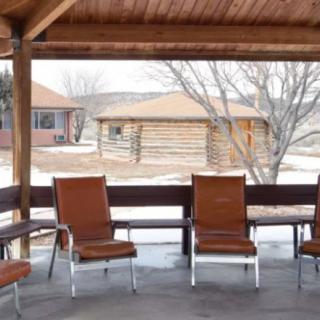 A wooden patio with chairs overlooks a snowy landscape and cabins.