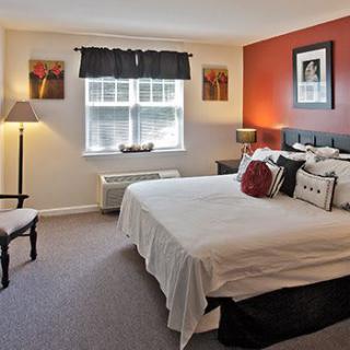 A cozy and well-decorated bedroom with a large bed, red accent wall, and natural light from the window.