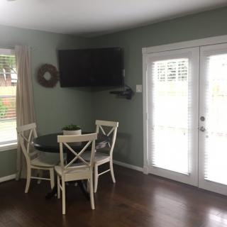 A cozy dining nook with a round table and chairs, featuring a wall-mounted television and bright French doors.