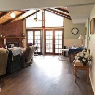 A cozy living room with a wooden ceiling, fireplace, and ample natural light streaming through French doors.