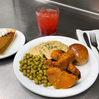 A dinner plate with turkey, gravy, peas, sweet potatoes, a roll, and a slice of pie served with a drink.