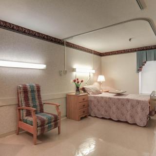 A well-lit hospital room with a bed, nightstand, and comfortable chair.