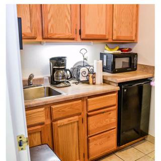 A compact kitchen with wooden cabinets, featuring a coffee maker and microwave on the countertop.