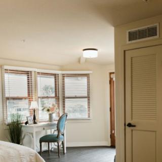 A cozy bedroom with a desk and chair by the window, featuring warm lighting and inviting decor.