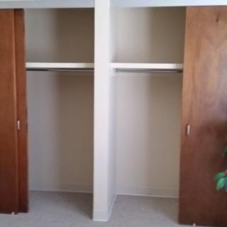 An empty closet with wooden sliding doors, featuring shelves and hanging space.