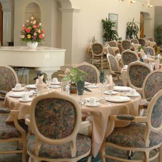 An elegant dining room with beautifully set tables and ornate chairs, featuring tasteful decor and a flower arrangement.