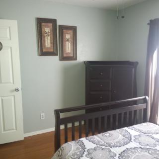 A neatly arranged bedroom with a bed, dresser, and wall art.
