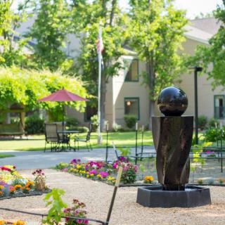 A scenic garden area with a sculpture, surrounded by flowers and trees.