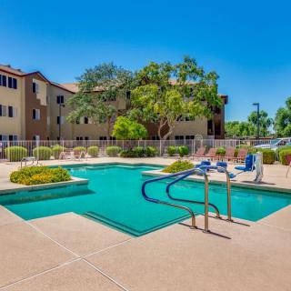 A sunny day at a residential apartment complex with a swimming pool surrounded by lush landscaping.