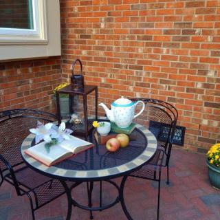 A cozy outdoor setting featuring a table adorned with tea, apples, and fresh flowers against a charming brick backdrop.