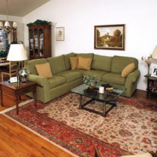 A cozy living room featuring a green sectional sofa, a glass coffee table, and decorative elements on the walls.