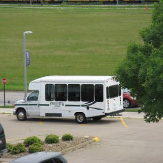 A white shuttle bus parked in a parking lot with a green field in the background.