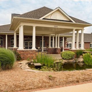 A charming brick house with a covered porch, surrounded by a landscaped garden with a small pond.