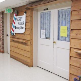 Entrance to a barber shop with wooden paneling and double white doors in a corridor.