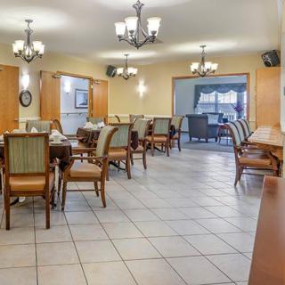 A well-lit dining area with multiple tables and chairs, featuring chandeliers and a tiled floor.