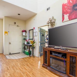 A cozy living room with wooden flooring, featuring a large television and stylish decor near the entryway.