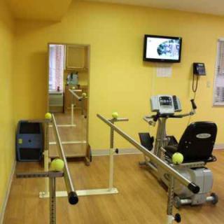 A rehabilitation room equipped with parallel bars, a stationary bike, and a mirror for physical therapy.