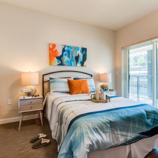 A modern bedroom with stylish decor, featuring a bed with blue and orange accents, bedside lamps, and contemporary artwork.