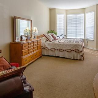A cozy bedroom with a large bed, wooden dresser, and ample natural light from the windows.